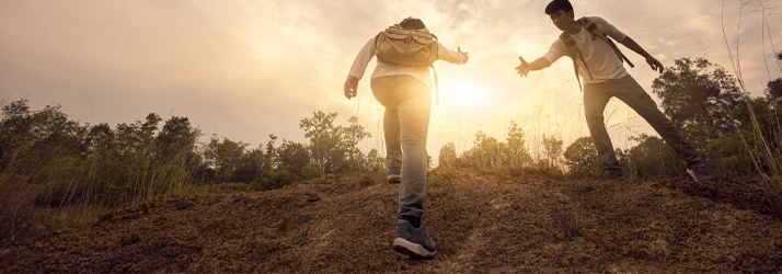 Two people walking on a hillside with one extending a hand toward the other near the top.