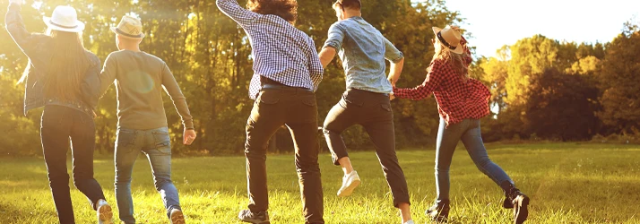 Four people running across a grassy field surrounded by trees in an outdoor setting.